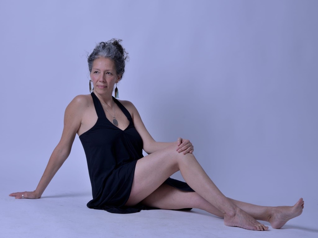 Nai sentada en el suelo, con un vestido negro, mirando a un lado